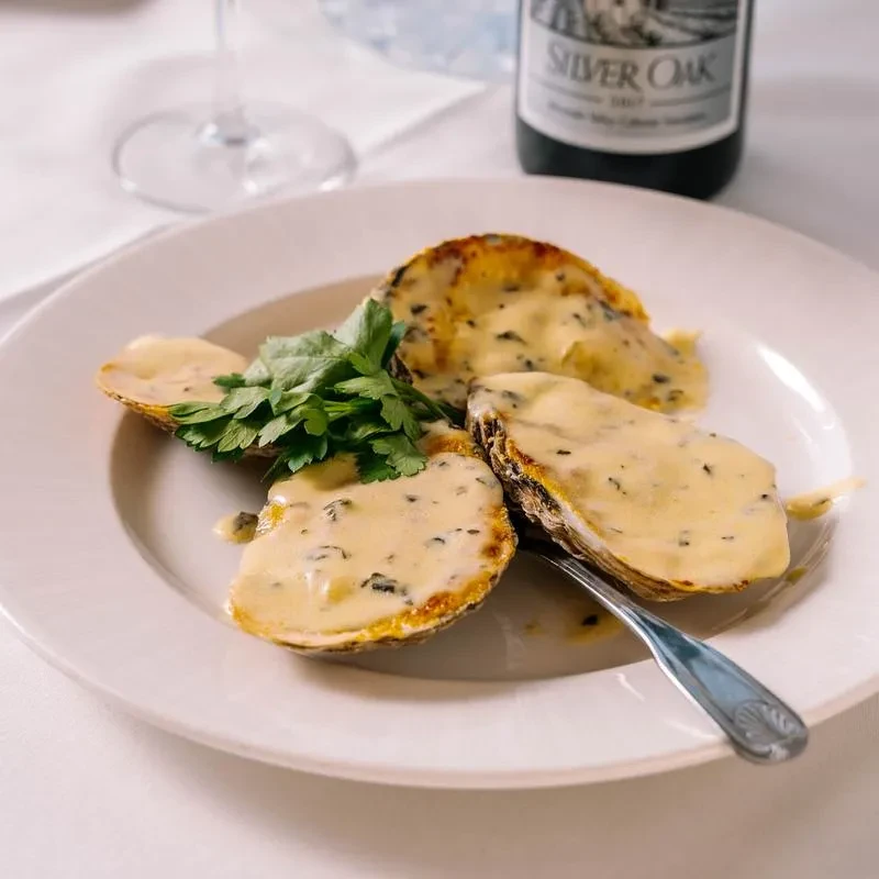 Baked oysters topped with creamy sauce, parsley, and a wine bottle.