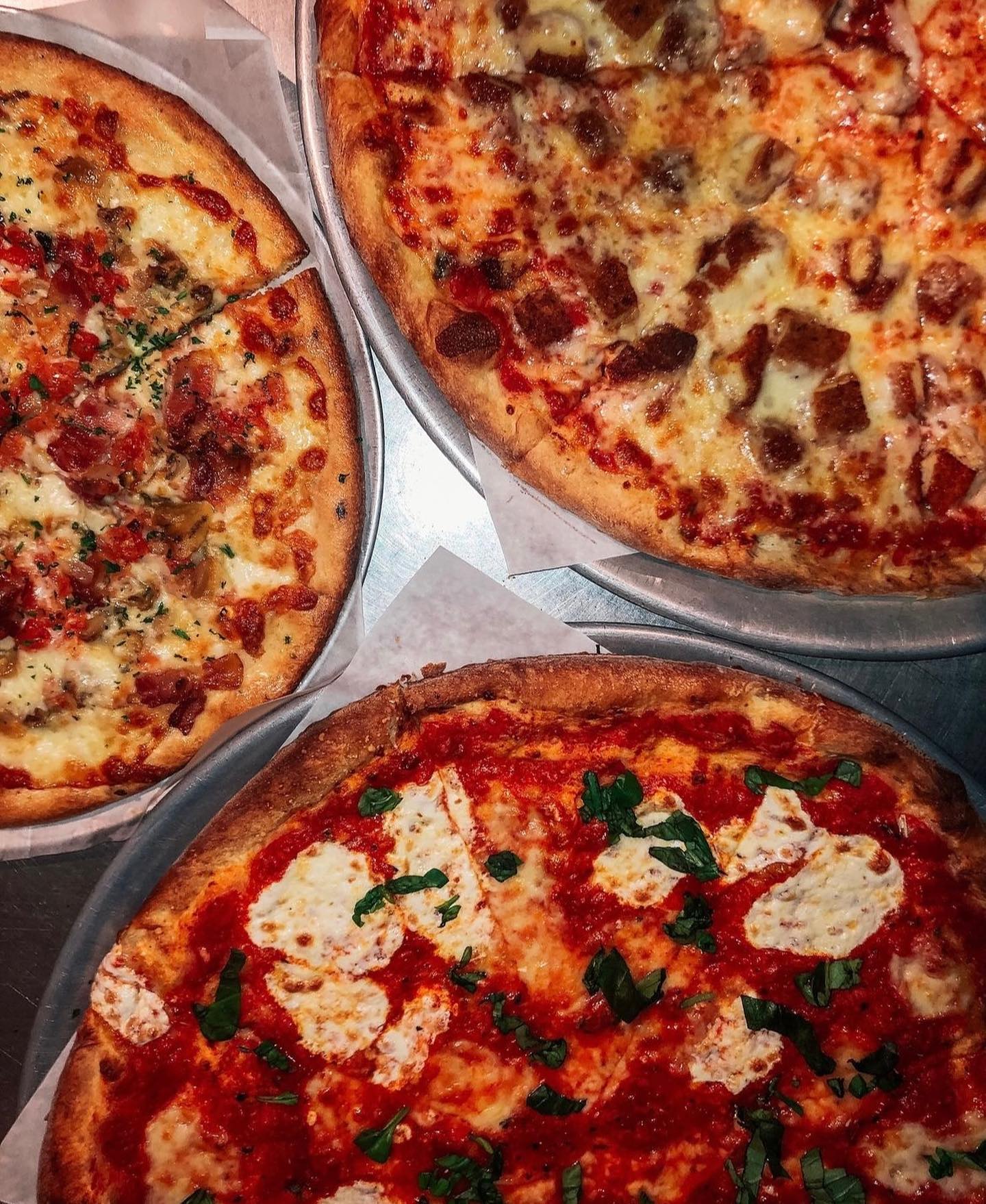 Three pizzas with various toppings on metal trays.