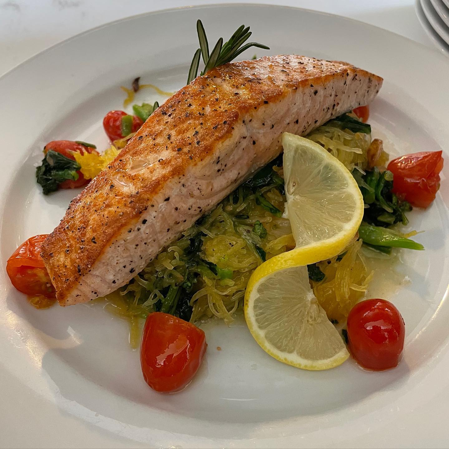 Cooked salmon on spaghetti squash, garnished with lemon, tomatoes, and rosemary.