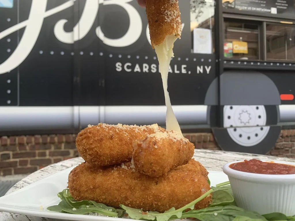 Cheese pull from a mozzarella stick in front of a food truck.