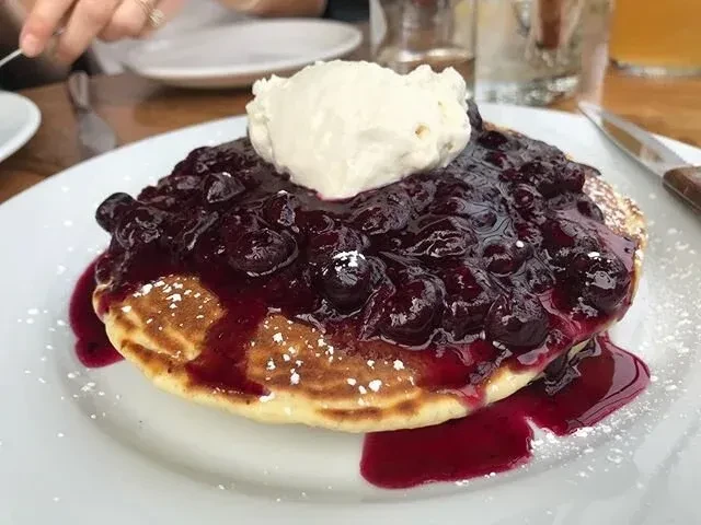 Pancake topped with blueberry compote, powdered sugar, and a dollop of cream.