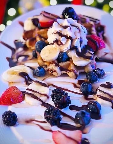Waffles topped with fruit, whipped cream, and chocolate syrup on a white plate.