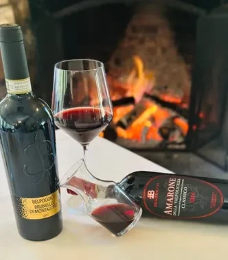 Bottles of red wine, a glass, and a decanter in front of a fireplace.
