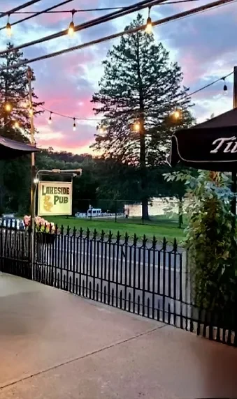 Lakeside Pub patio at sunset with string lights, fence, and water.
