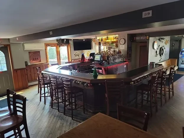Empty bar interior with U-shaped wooden counter, lit liquor shelf, and decor.
