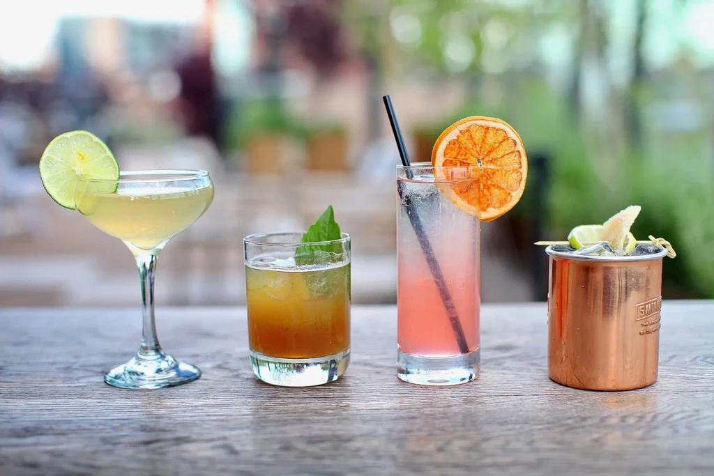 Four cocktails on a wooden table, garnished with fruit and mint.