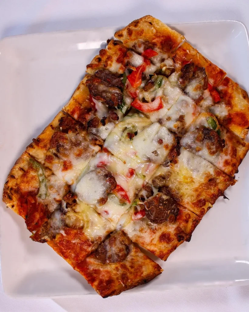 A rectangular pizza with melted cheese, sausage, and peppers on a white plate.
