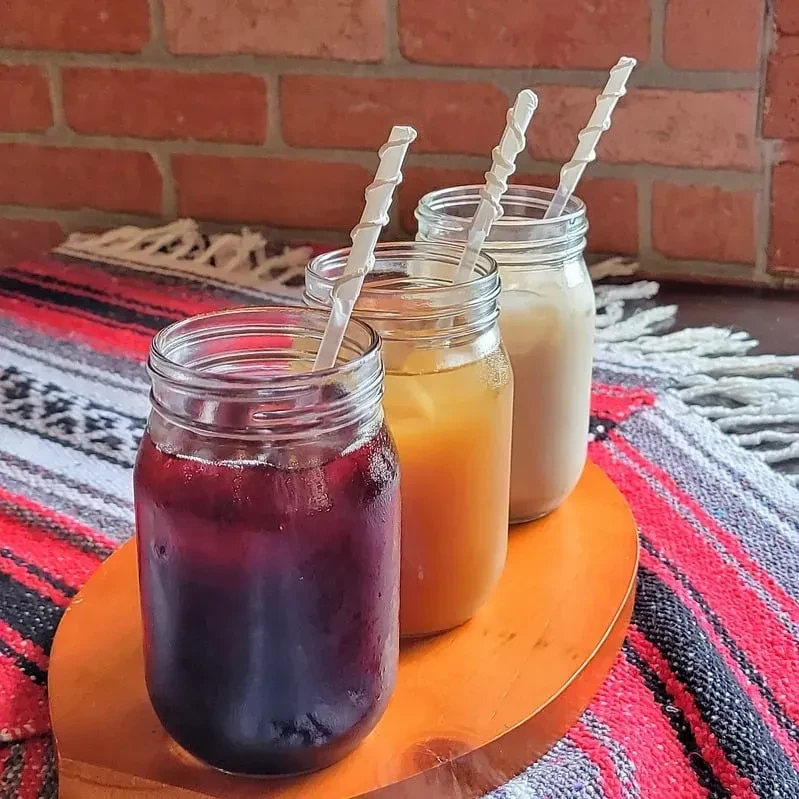 Three glasses of iced drinks with straws on a wooden tray.