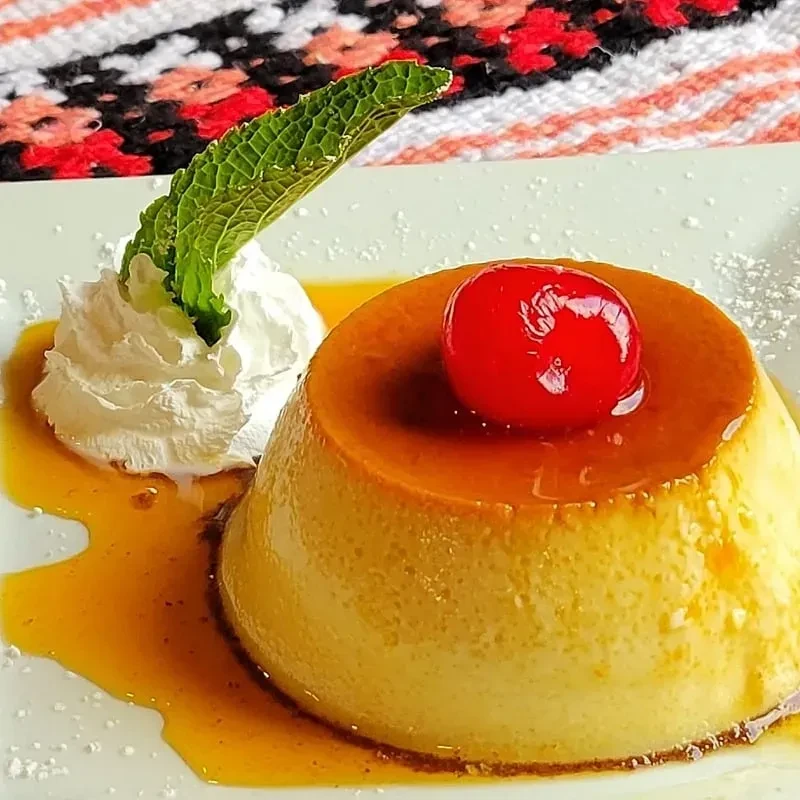 Flan with caramel sauce, whipped cream, a cherry, and a mint leaf.