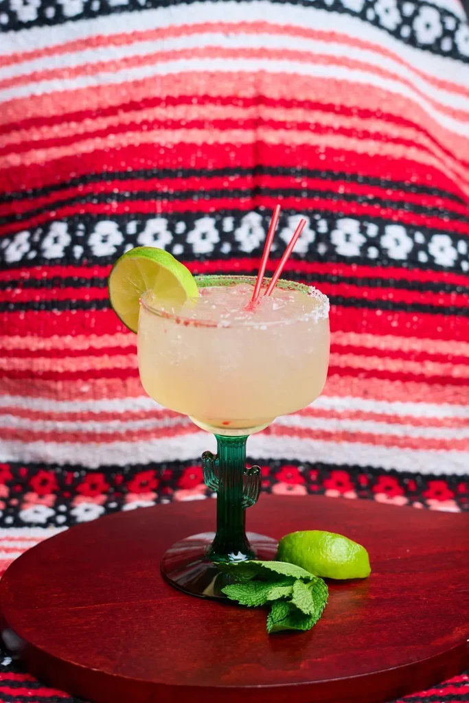 Margarita in a cactus glass with lime and mint on a wooden board.