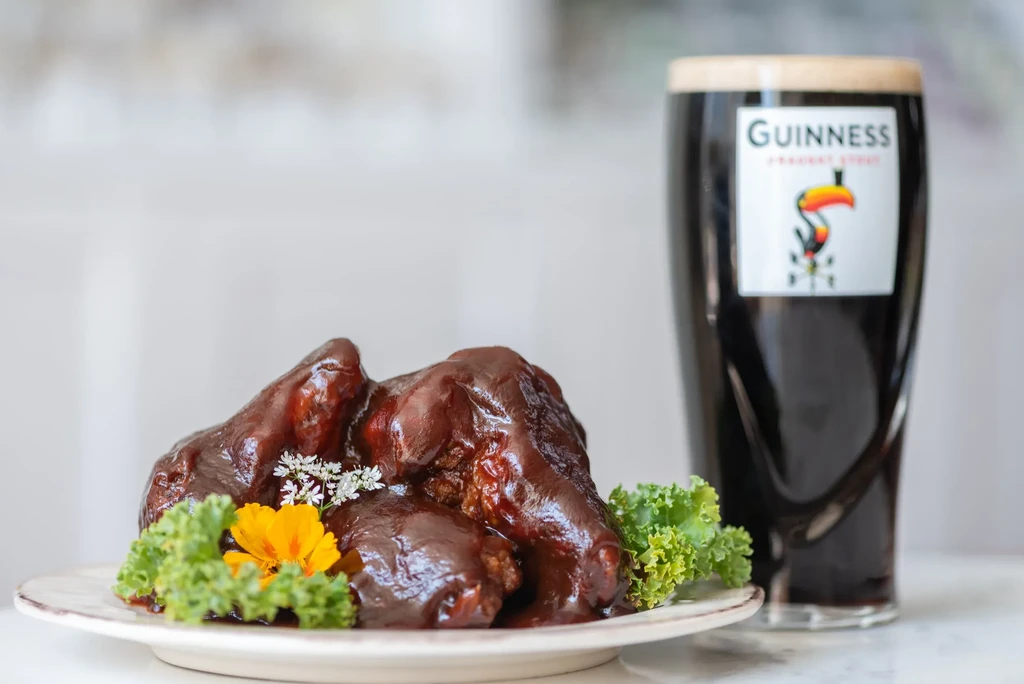 Saucy chicken wings, garnished with kale and flowers, next to a Guinness beer.
