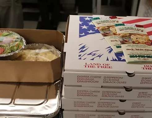 Stack of pizza boxes next to a box of salad and baked goods.