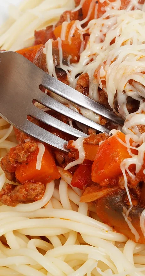 A fork lifts cheesy spaghetti with meat sauce and vegetables.