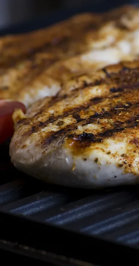 Grilled chicken breast with char marks on a dark griddle.