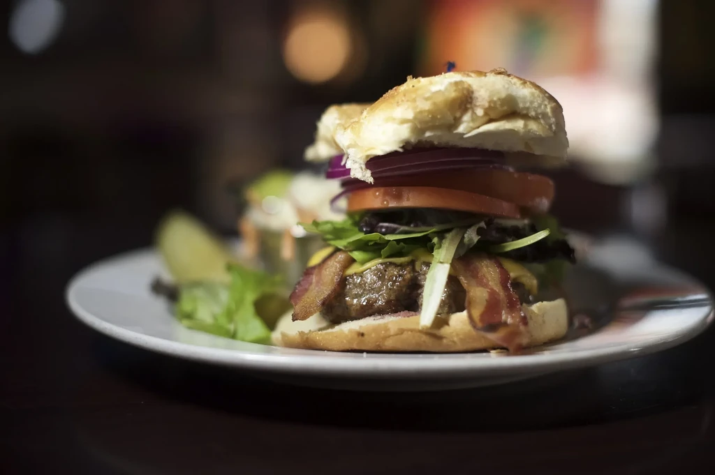 A bacon cheeseburger with tomato and onion on a white plate.
