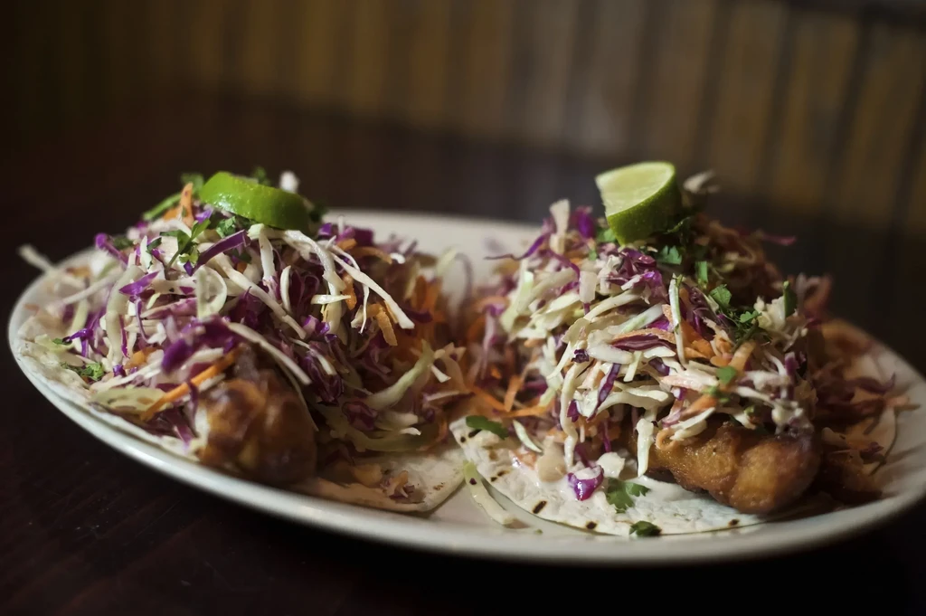 Two fish tacos with slaw, cilantro, and lime on a white plate.
