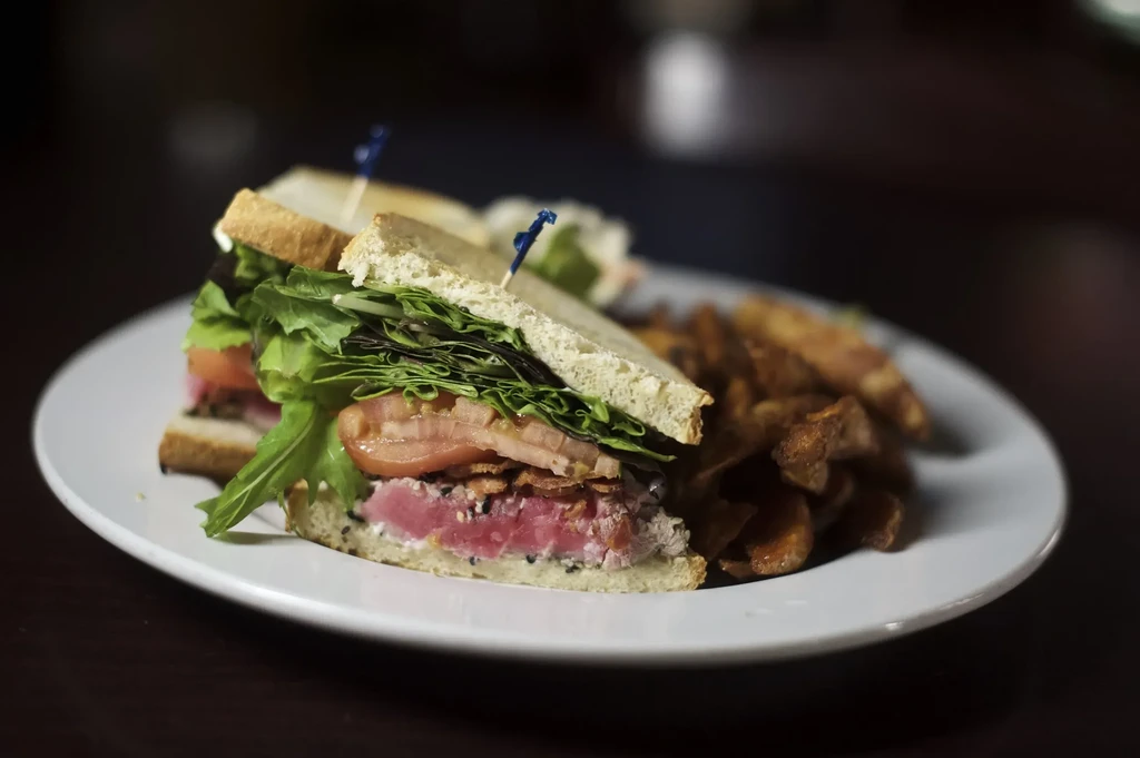 Seared tuna club sandwich with lettuce, tomato, bacon and potato wedges.