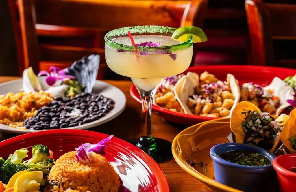 A table full of colorful Mexican food and a margarita.