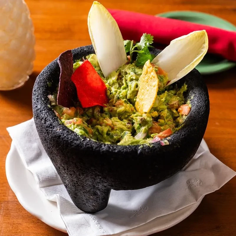 Guacamole served in a black stone molcajete with chips and endive.