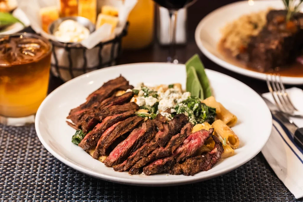 Sliced steak with pasta, spinach, and blue cheese on a white plate.