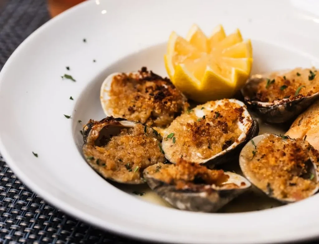 Baked clams with breadcrumbs and parsley, garnished with carved lemon.