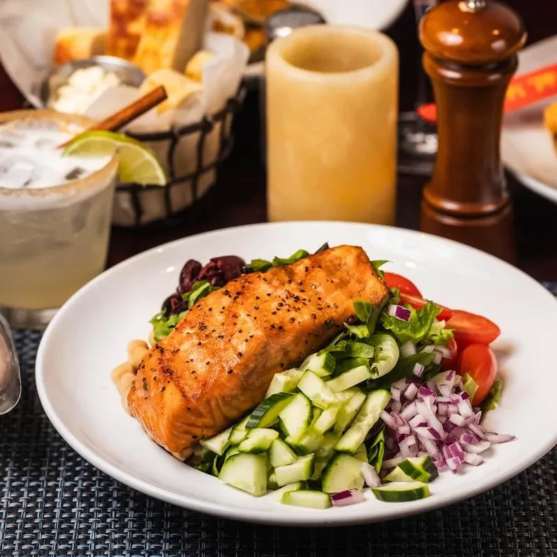 Salmon with salad, margarita, and bread basket on a dark table.