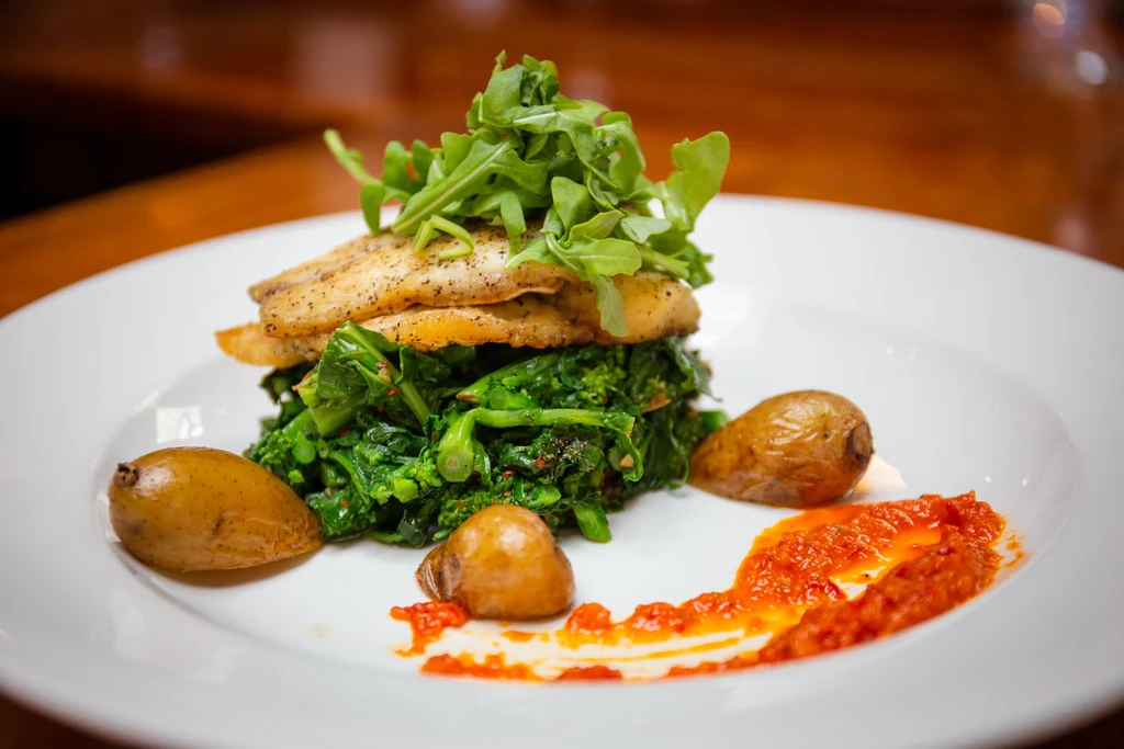Pan-fried fish with greens, roasted potatoes, and red sauce on a plate.