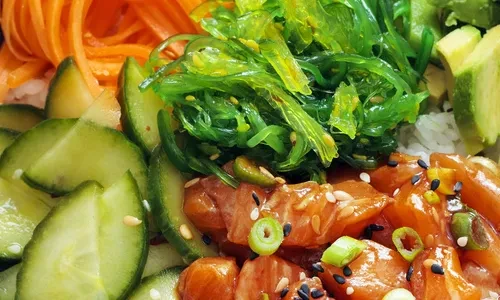 Close-up of a poke bowl with salmon, seaweed, carrots, and cucumbers.