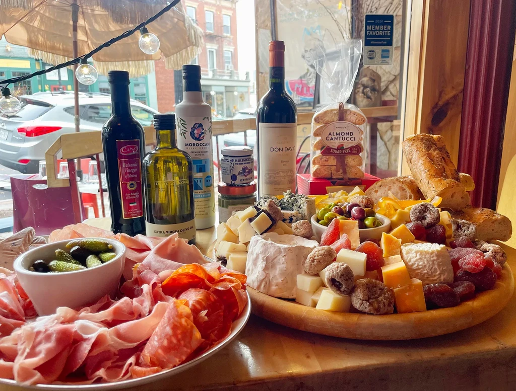 A charcuterie board with cheese, meat, olives, bread, and wine bottles.