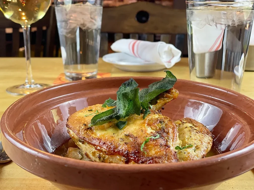 A close-up of a chicken dish with sage in a brown bowl.