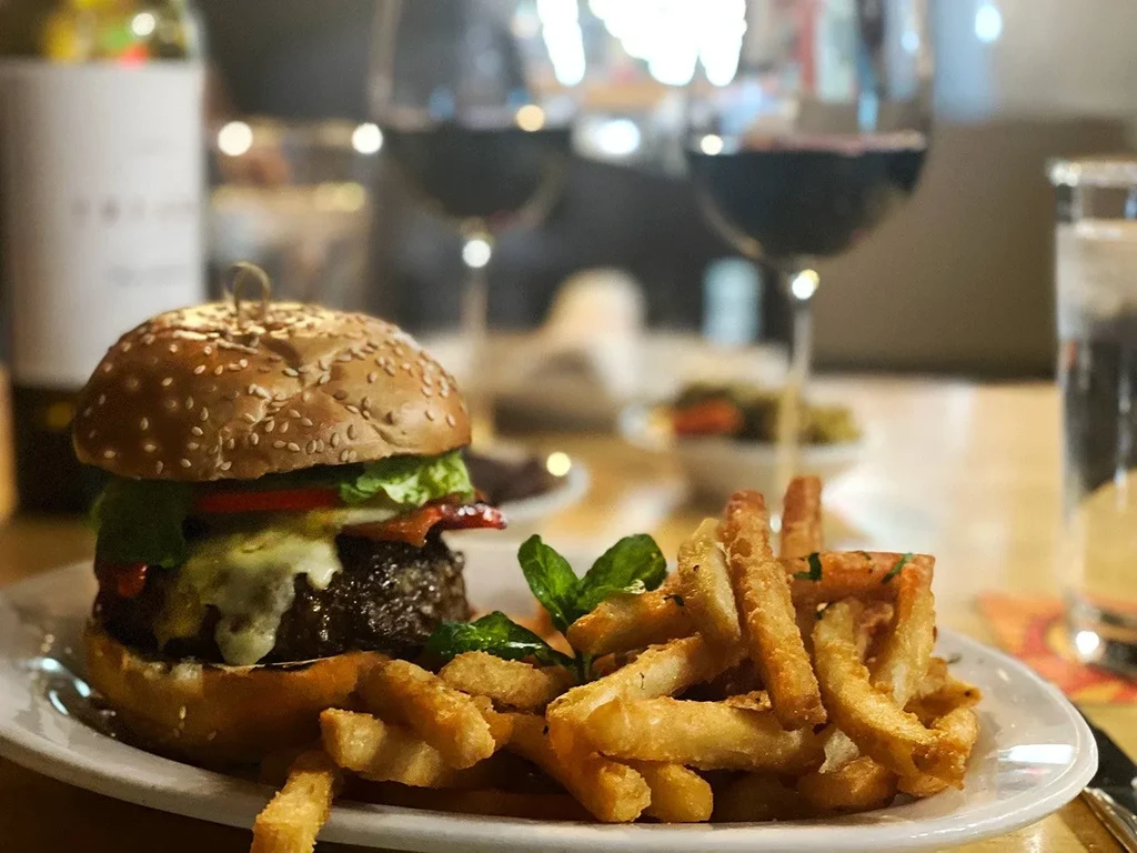 A gourmet burger and french fries with wine on a restaurant table.