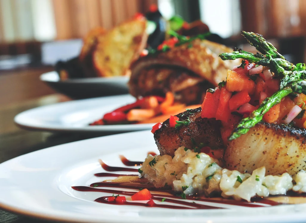 Seared scallops with risotto, tomato salsa, and asparagus on a white plate.
