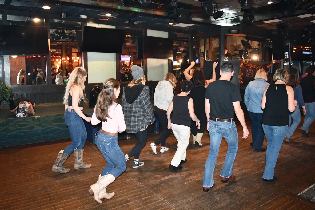 Energetic group line dancing in a dimly lit country bar.