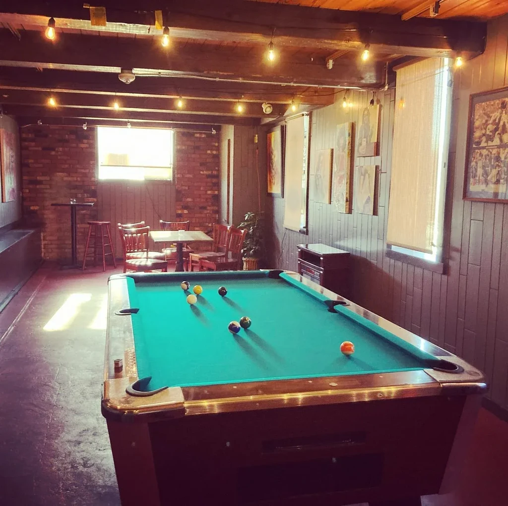 Rustic lounge with a turquoise pool table and Edison string lights.