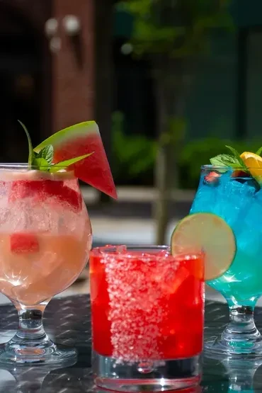 Three colorful cocktails, one pink, one red, and one blue, on a table.