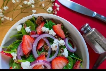A spinach salad with strawberries, red onions, pecans, and feta cheese.