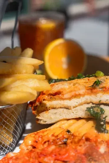 Close-up of a sandwich, fries, and beverage with an orange slice.