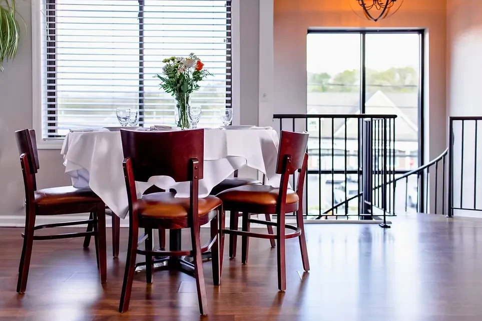Empty dining table set with flowers and place settings by a window.