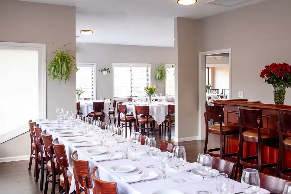 Formal restaurant dining room with long table, bar, and round tables.