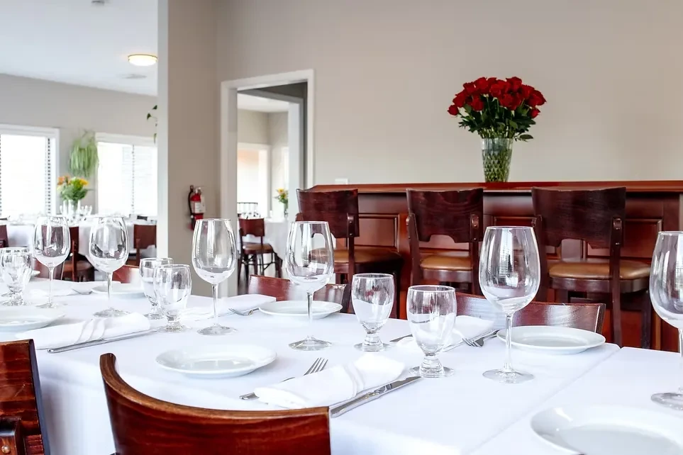 Elegantly set restaurant table with white linens, glasses, and red roses.