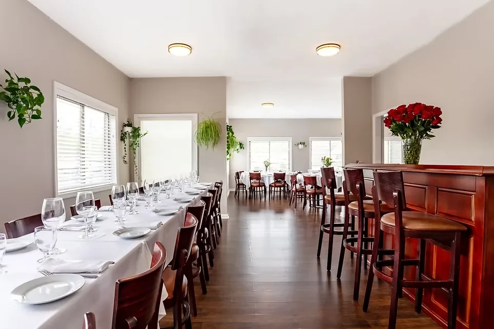 Bright, elegant restaurant interior with set tables and a dark wood bar.