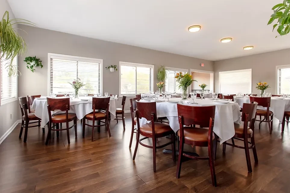 Empty dining room with uniformly set tables, plants, and natural light.