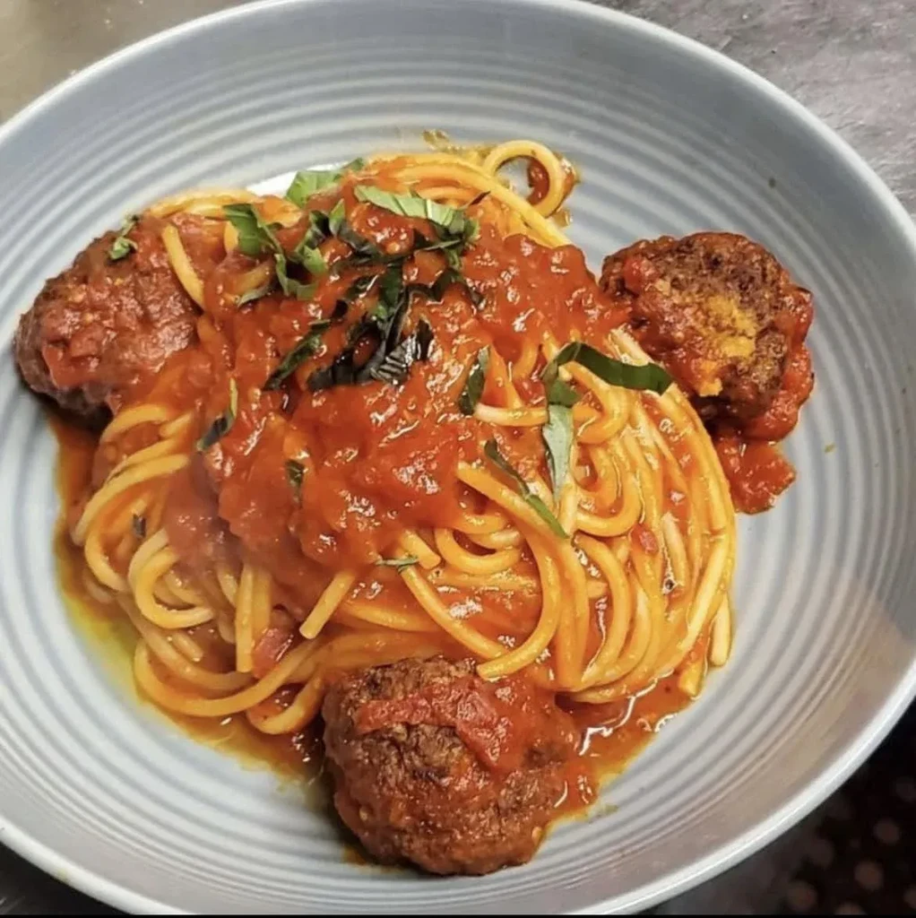 A bowl of spaghetti with meatballs, tomato sauce, and basil.