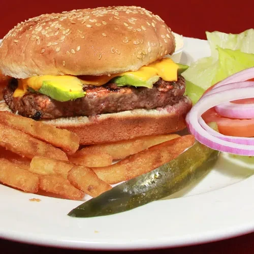 A burger with avocado, french fries, and dill pickle spear.