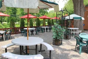 Gravel patio with white picnic tables, green chairs, and umbrellas.