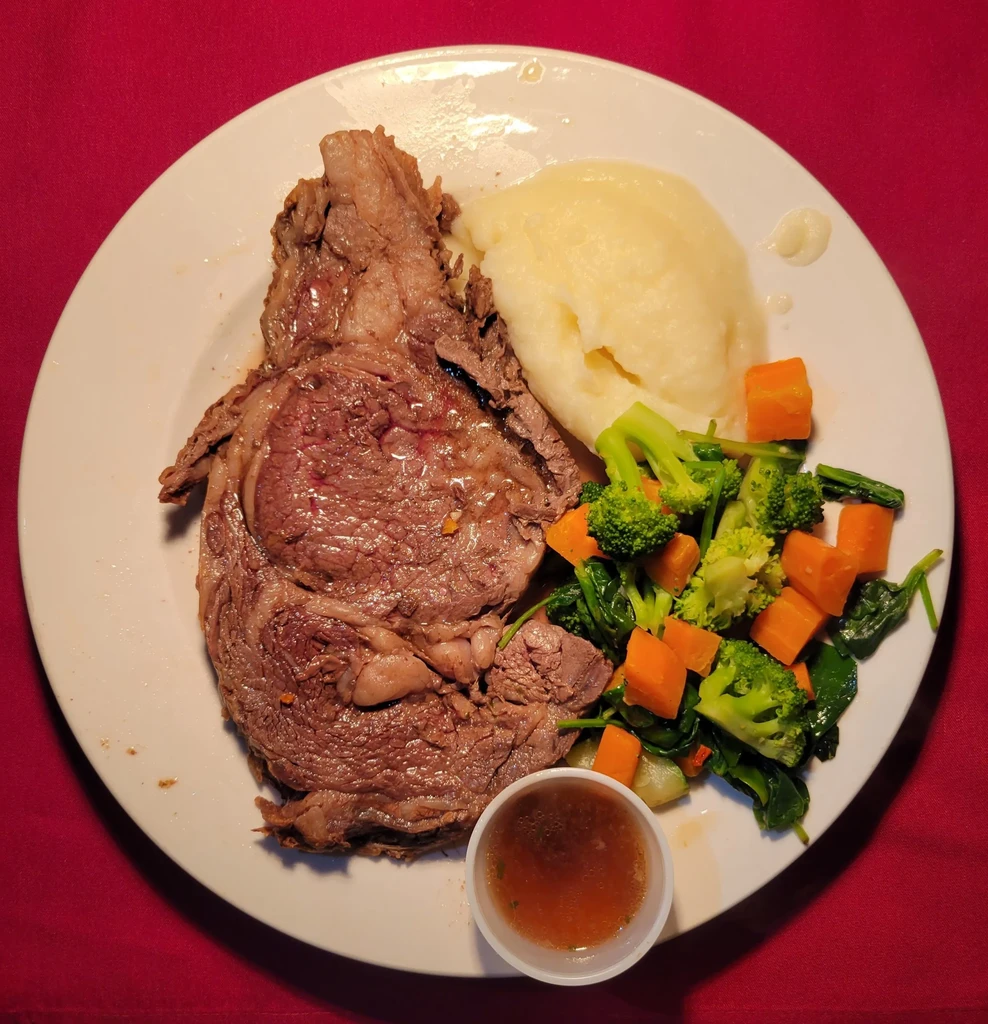 Well-plated prime rib, mashed potatoes, vegetables, and sauce.