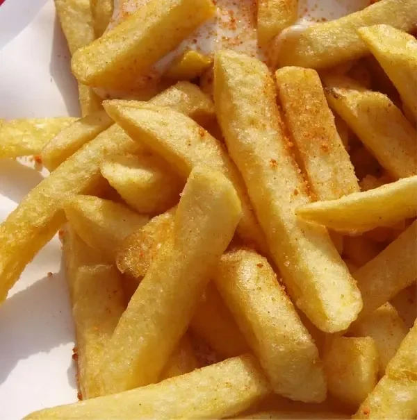 Close-up of seasoned golden-brown thick-cut french fries with dipping sauce.