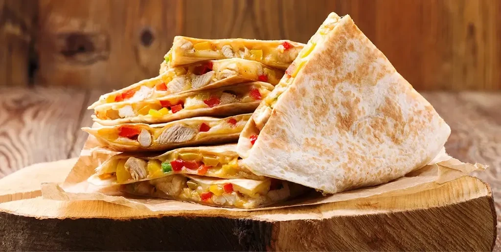 Triangular quesadillas with chicken, cheese, and peppers on a wooden log slice.