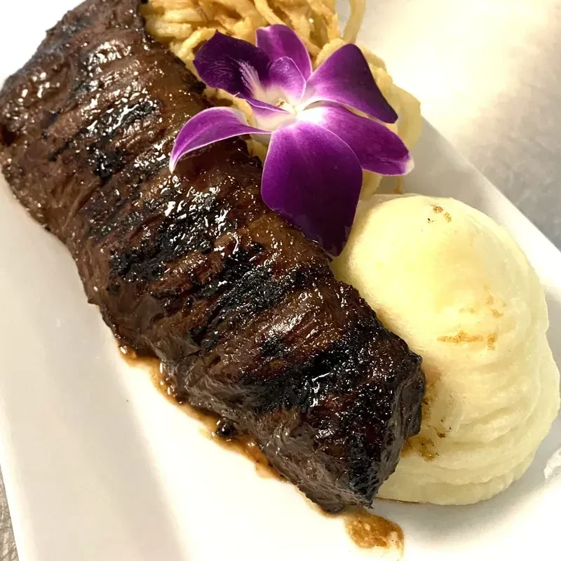 Grilled steak with mashed potatoes, crispy onions, and a purple orchid.