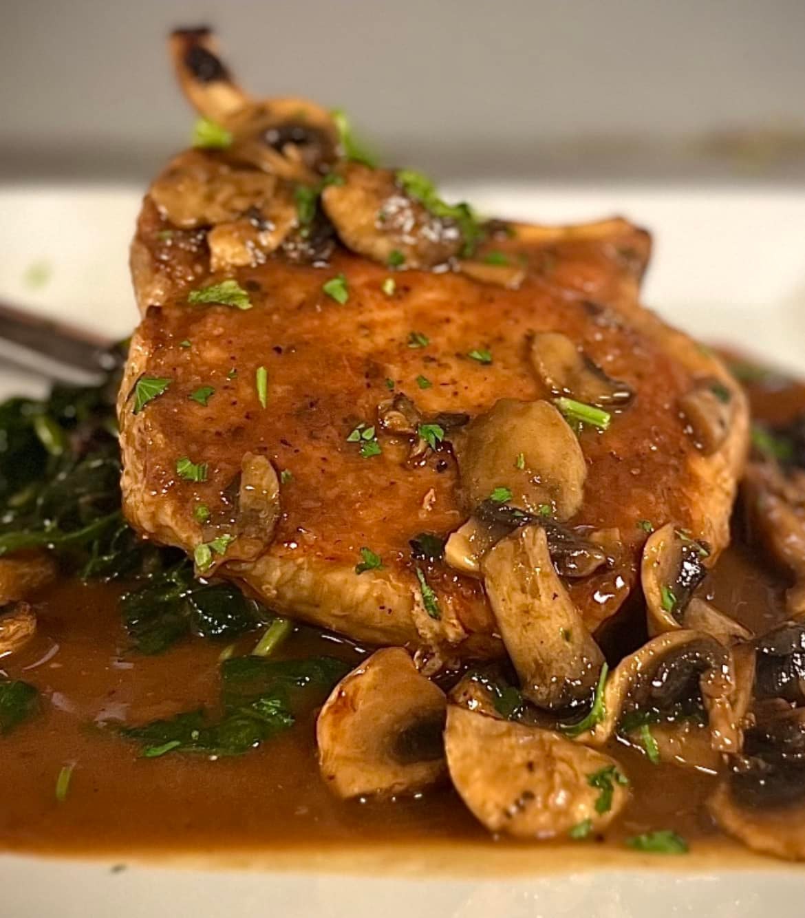 Bone-in pork chop with mushroom sauce, spinach, and parsley.